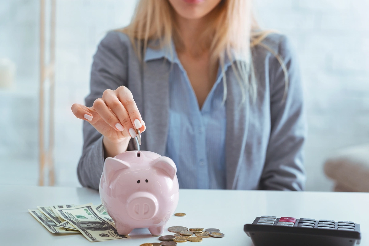 Mujer depositando monedas en una hucha rosada mientras aplica tips para ahorrar dinero en casa.