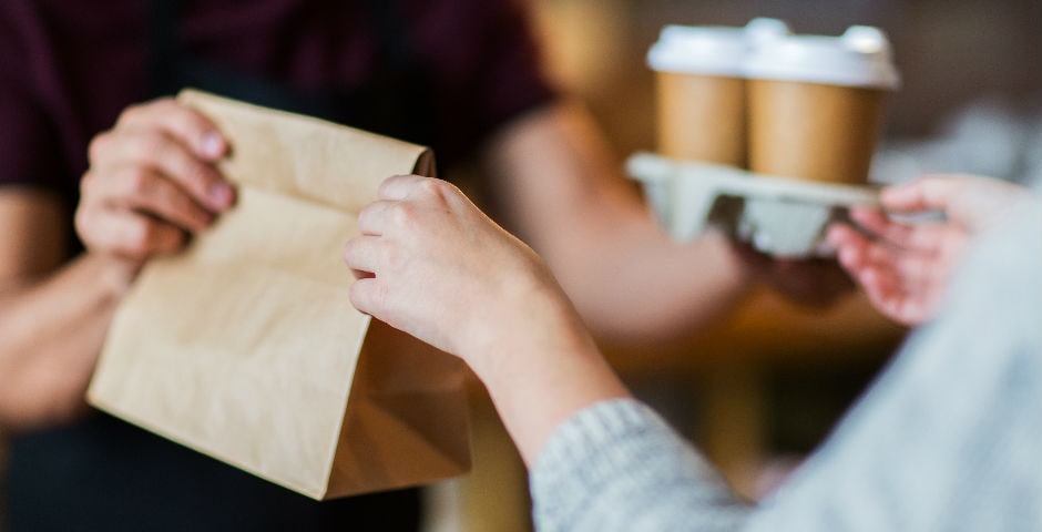 Mans intercanviant una bossa de paper i cafès, exemplificant les despeses formiga diàries.