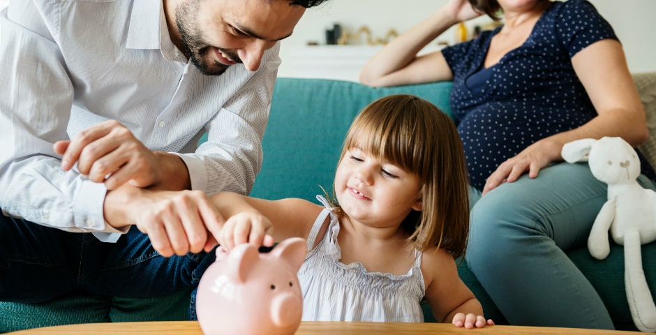 Pare ajudant la seva filla a estalviar diners en una guardiola, fomentant l'estalvi infantil en família.