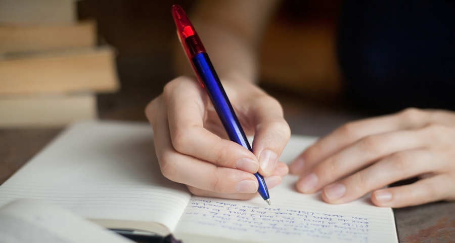 Mano escribiendo a mano con bolígrafo azul en un cuaderno, reflejando la evolución de la caligrafía.