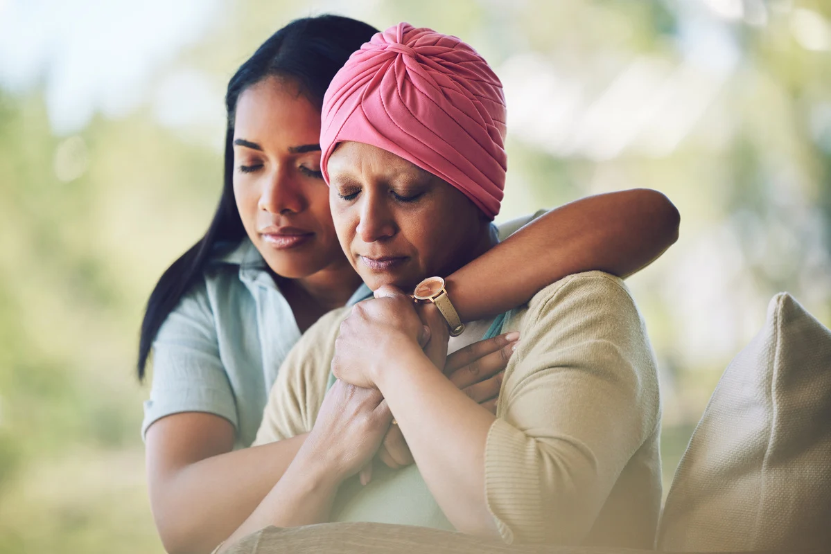Mujer joven abrazando a una mujer mayor con turbante rosa, mostrando el apoyo emocional y cuidado integral durante el tratamiento del cáncer.