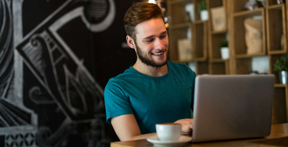 Joven autónomo trabajando con su portátil en una cafetería, disfrutando de un ambiente relajado.