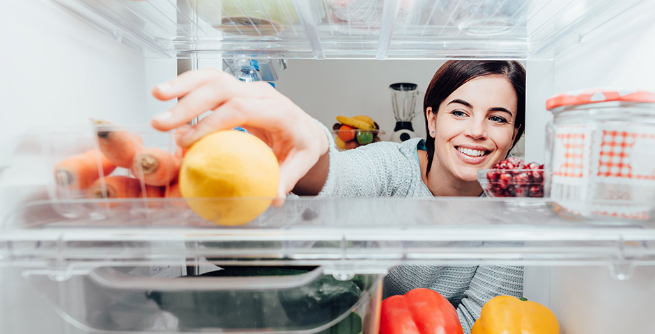 Mujer organizando alimentos en la nevera, aplicando consejos para ahorrar energía.