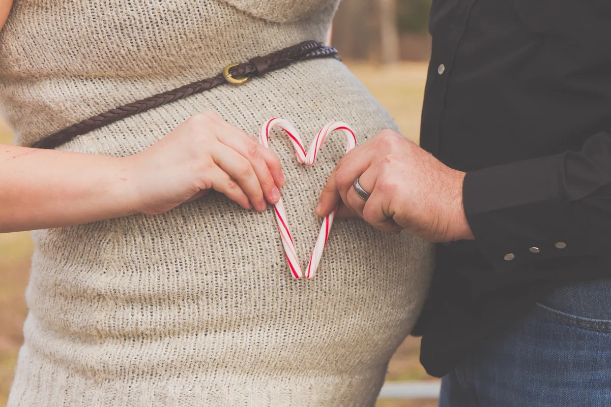 Pareja formando un corazón con bastones de caramelo, simbolizando permisos y bajas por maternidad y paternidad.