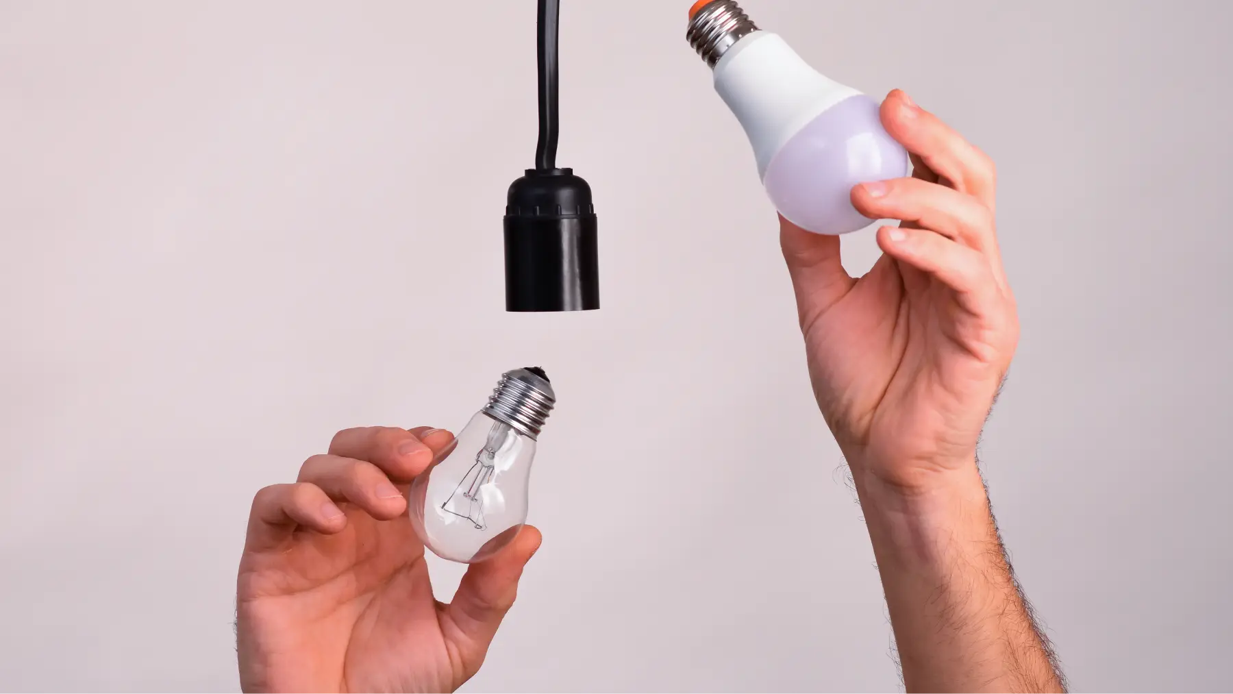 Manos cambiando una bombilla tradicional por una LED para fomentar el ahorro de energía.