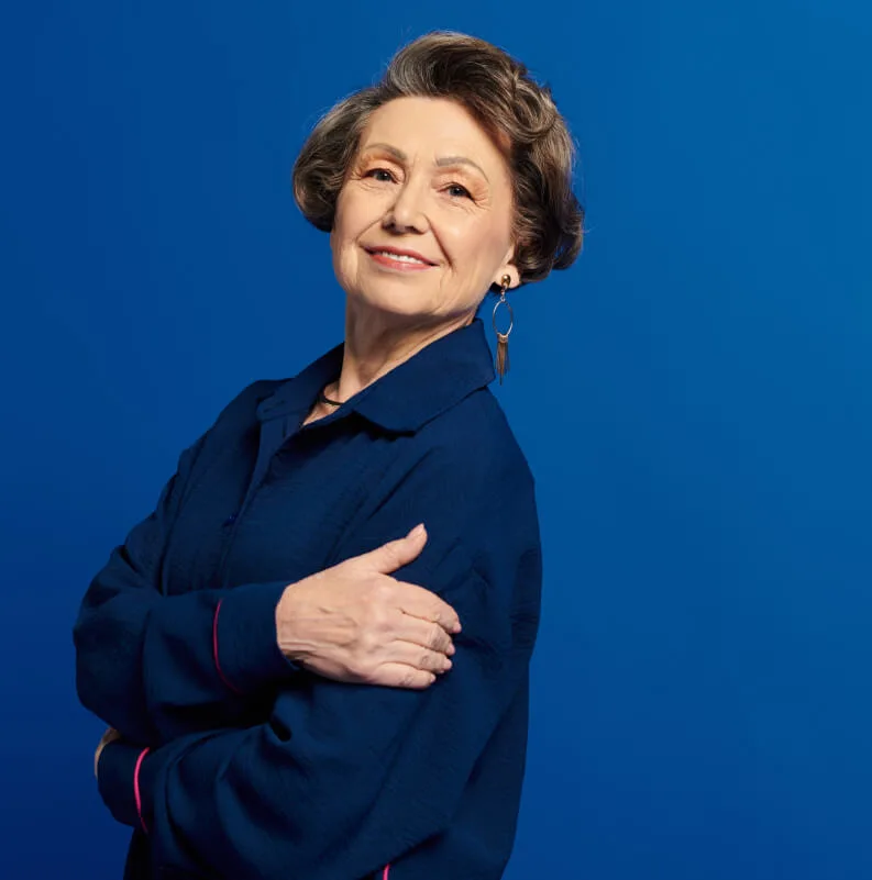 Mujer mayor sonriente y segura de sí misma sobre fondo azul, representando la vitalidad y la opción de la jubilación demorada a los 70 años.