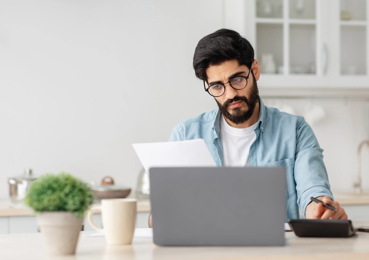 Hombre joven con gafas revisando documentos en ordenador, ilustrando la solicitud del certificado de Seguridad Social.