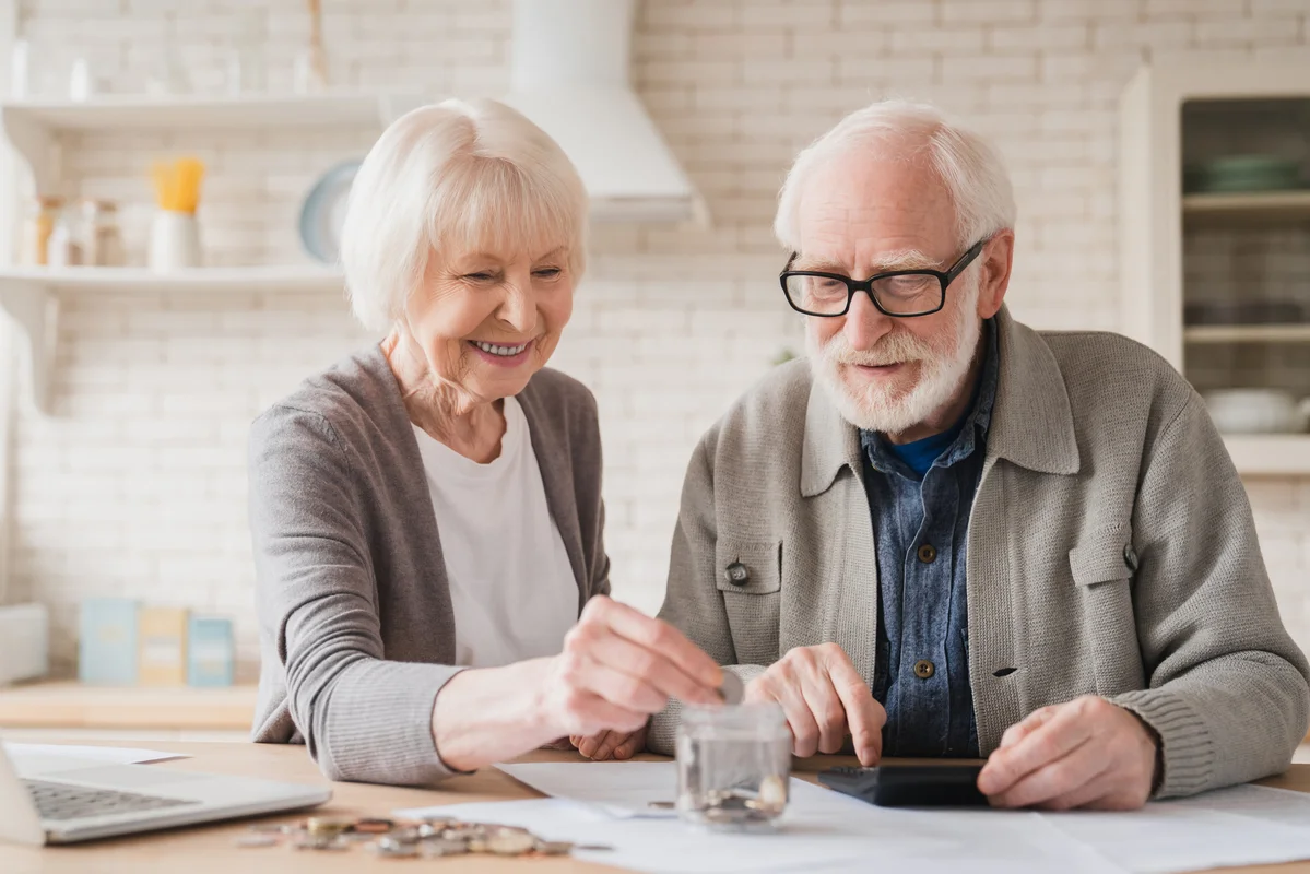 Dues persones grans posant monedes en un pot mentre es plantegen si és compatible la pensió amb l'ajuda a la dependència
