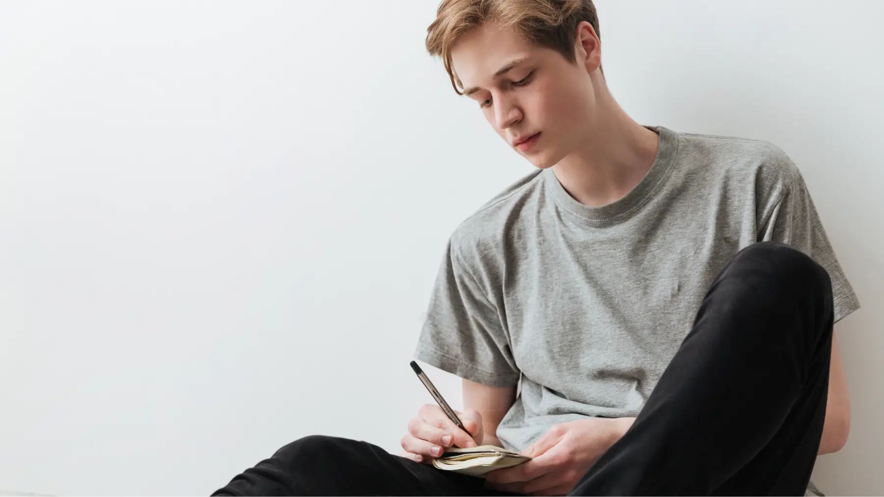 Un joven pensativo escribe, considerando contratar un seguro de vida para proteger su futuro.