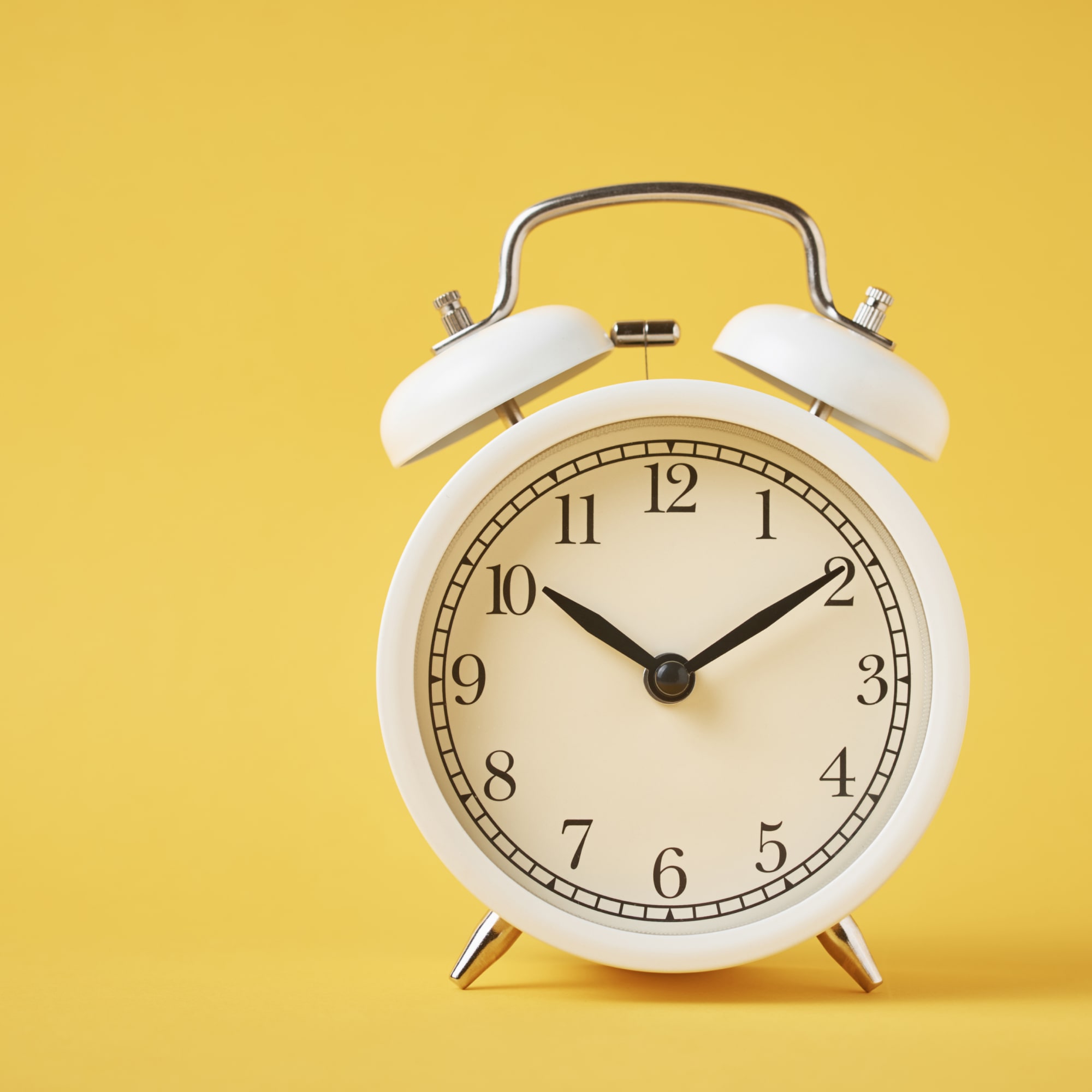 Reloj despertador blanco sobre fondo amarillo, simbolizando el tiempo necesario para jubilarse. 