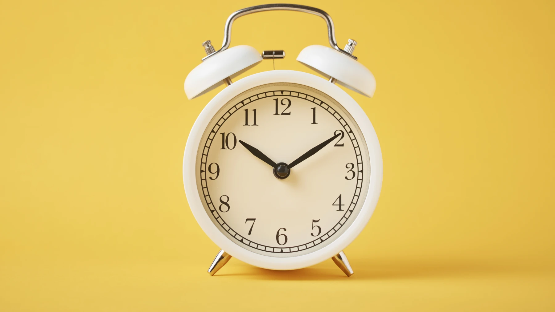 Reloj despertador blanco sobre fondo amarillo, simbolizando el tiempo necesario para jubilarse. 