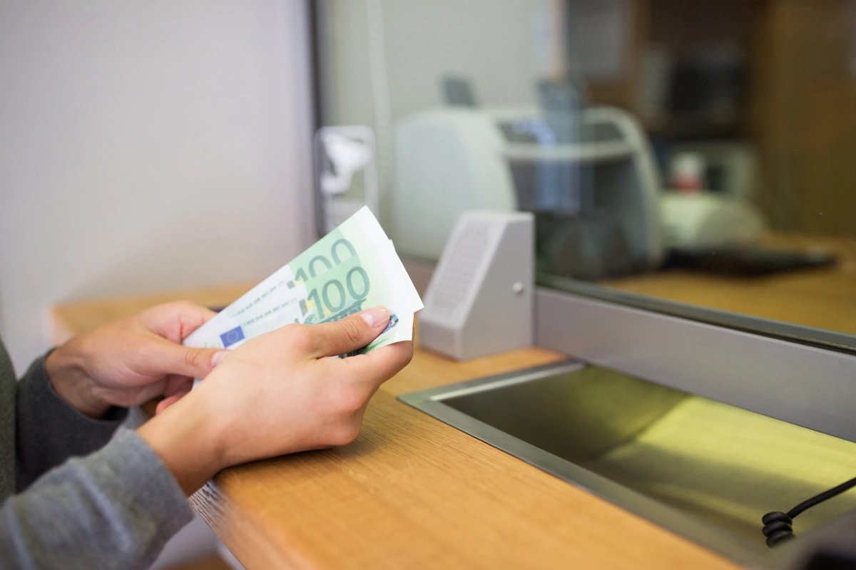 Persona contando billetes en ventanilla bancaria, comparando depósito bancario vs seguro de ahorro.