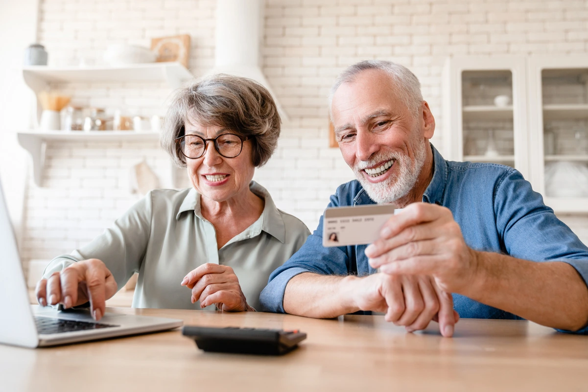 Pareja de jubilados comprando en línea con tarjeta, aprovechando descuentos para mayores de 60 y 65 años.