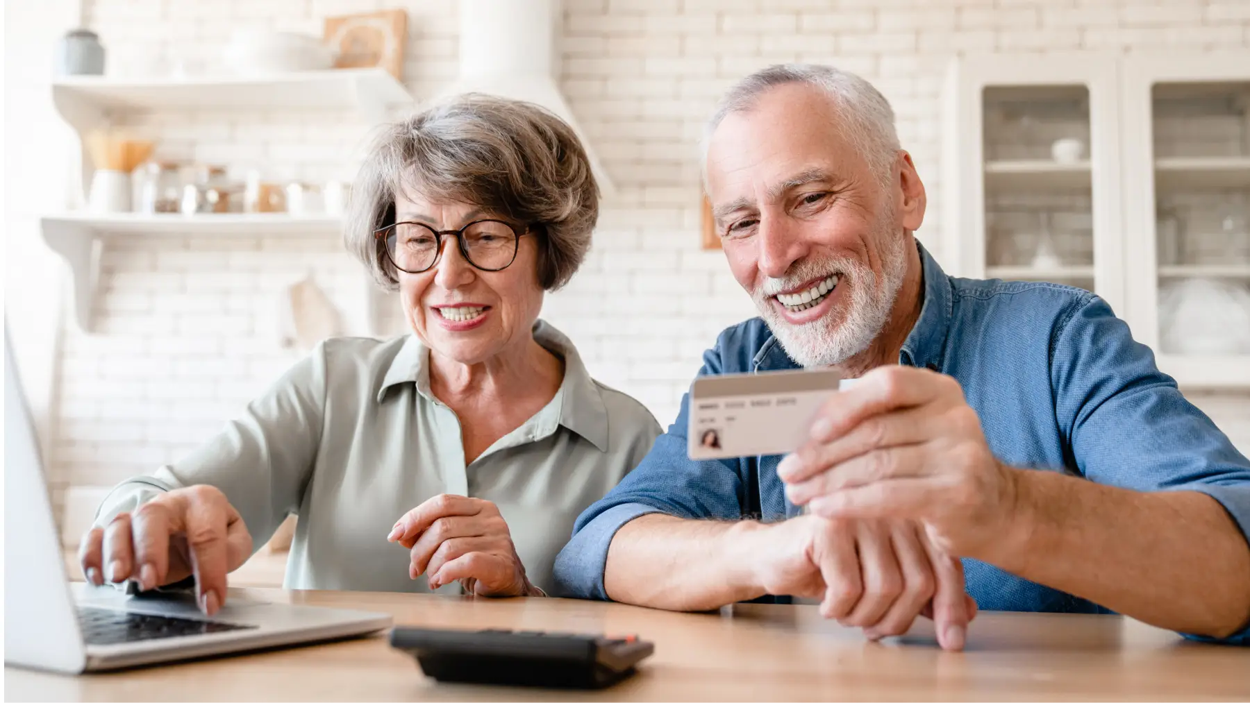 Pareja de jubilados comprando en línea con tarjeta, aprovechando descuentos para mayores de 60 y 65 años.