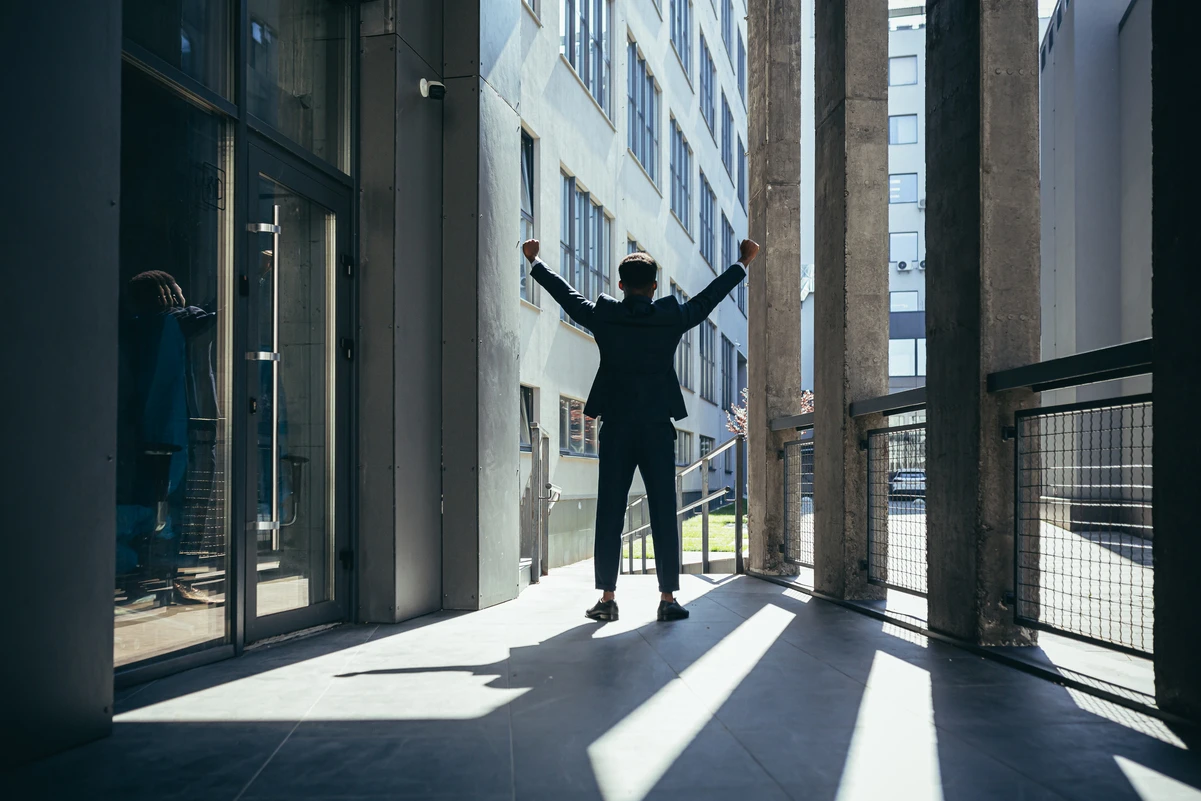 Hombre saliendo de un edificio con brazos en alto, representando el día exacto de su jubilación.