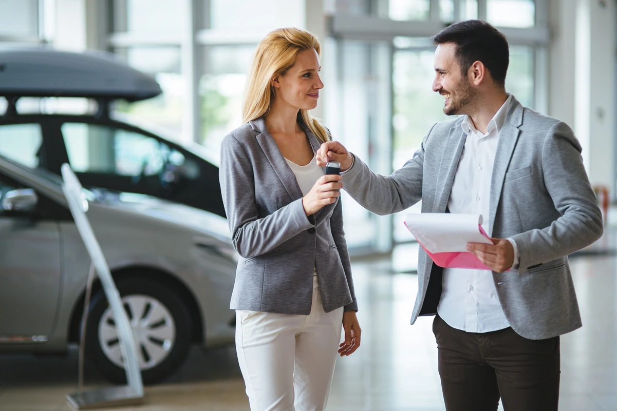 Mujer sonriente recibiendo llaves de coche, representando la relación entre dinero, compras y felicidad.