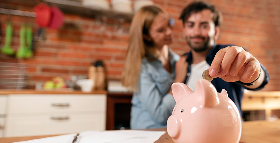 Pareja sonriente ahorrando dinero juntos en una hucha en forma de cerdito.