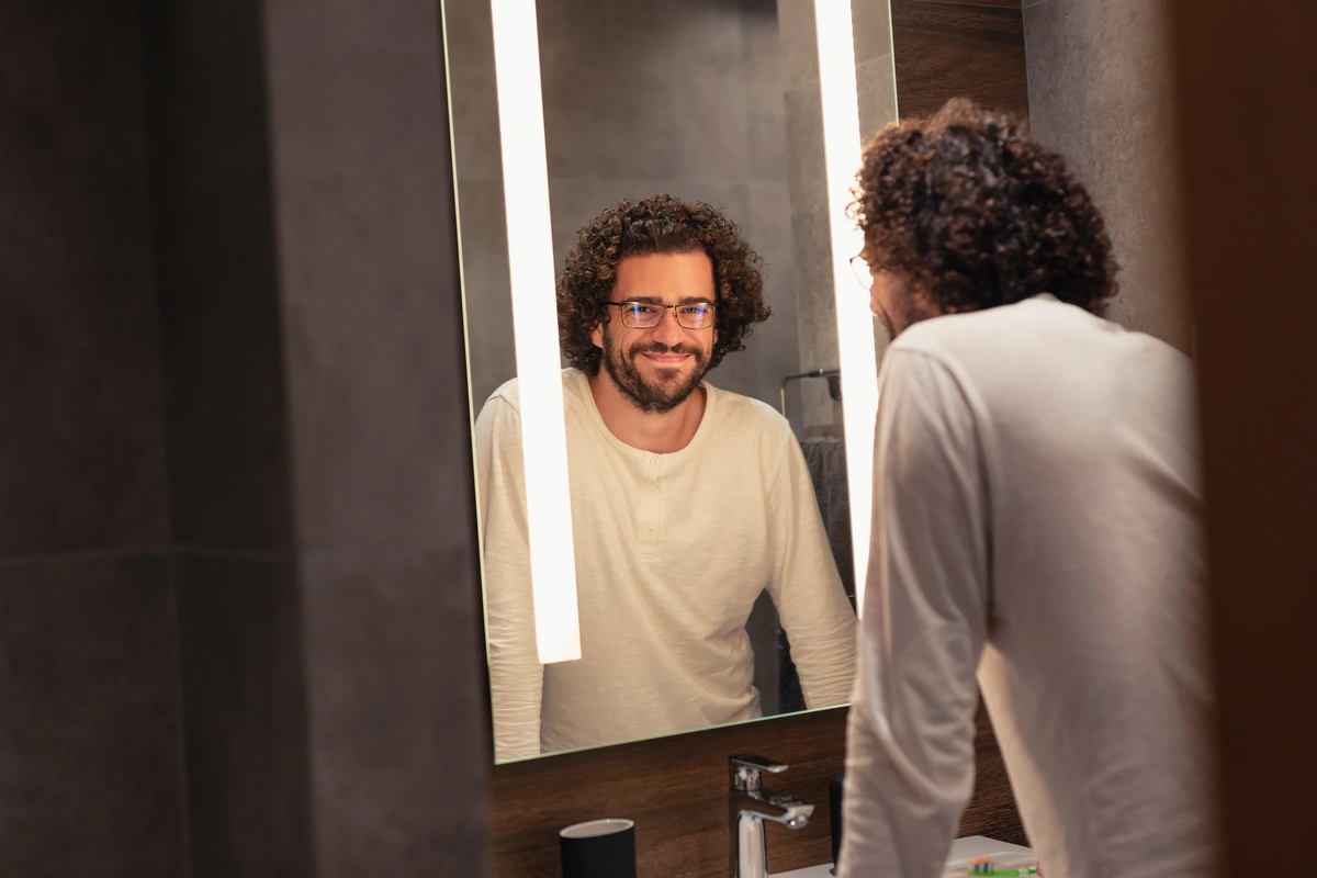 Un hombre adulto sonríe frente al espejo, reflexionando sobre a qué edad se es anciano según la OMS.