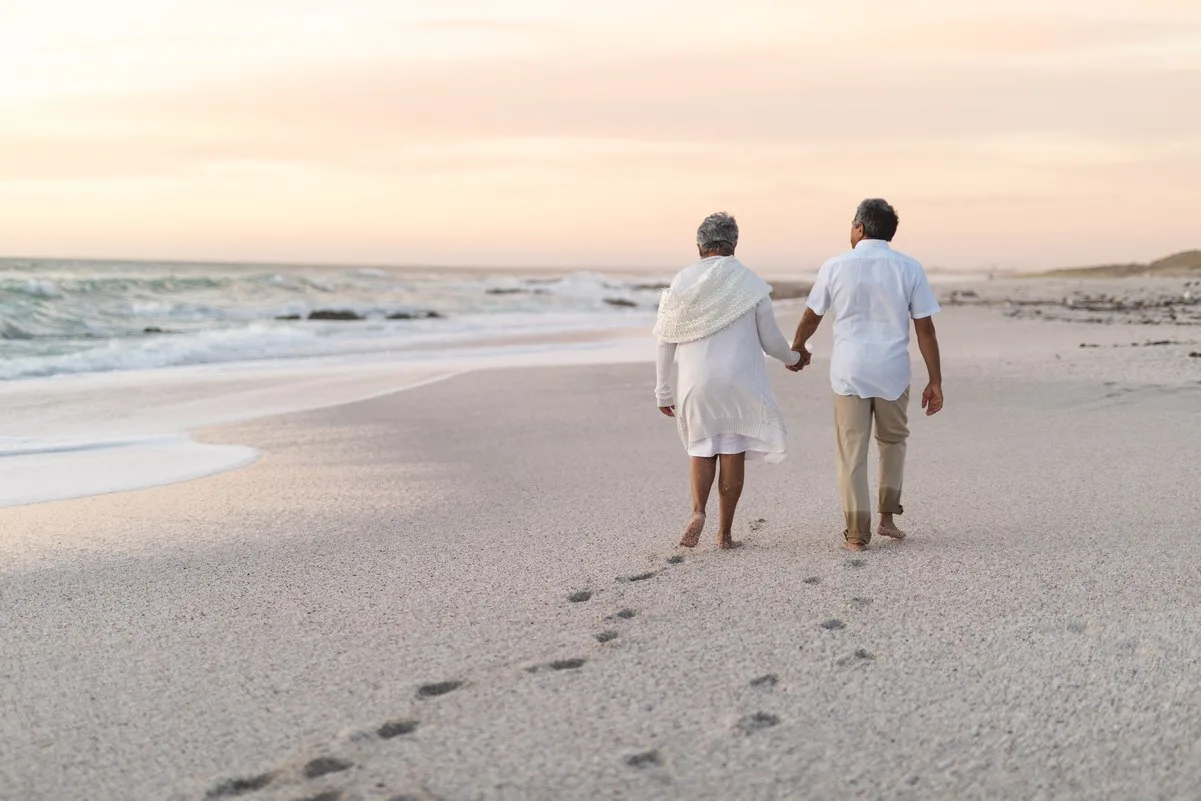 Pareja de jubilados caminando por la playa, simbolizando el impacto de una excedencia en la pensión.