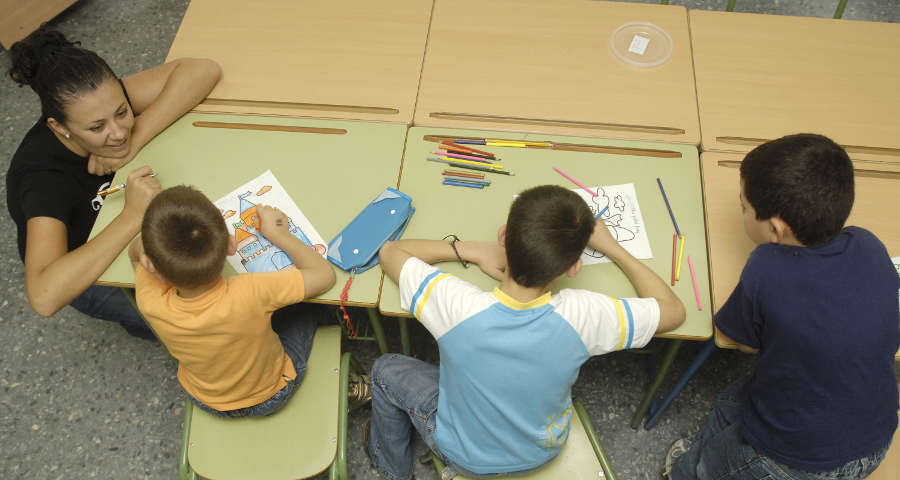Docente observando a tres niños mientras colorean en clase, representando la jubilación de funcionarios docentes.