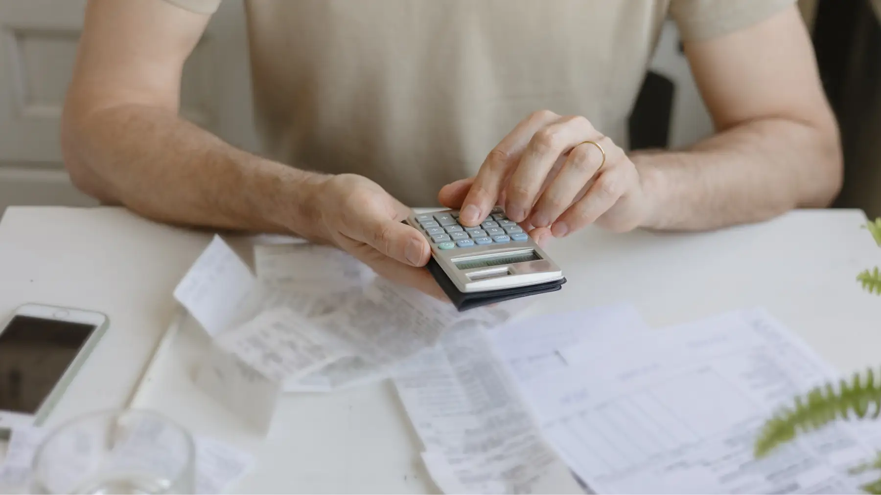Hombre usando calculadora y revisando documentos, simbolizando cómo transformar pequeños ahorros en grandes.