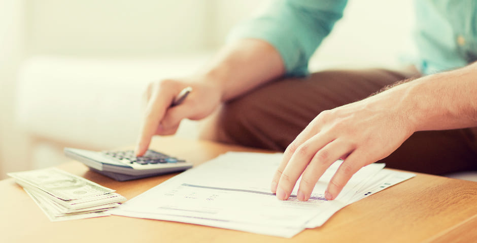 Hombre usando calculadora y revisando documentos, simbolizando cómo transformar pequeños ahorros en grandes.
