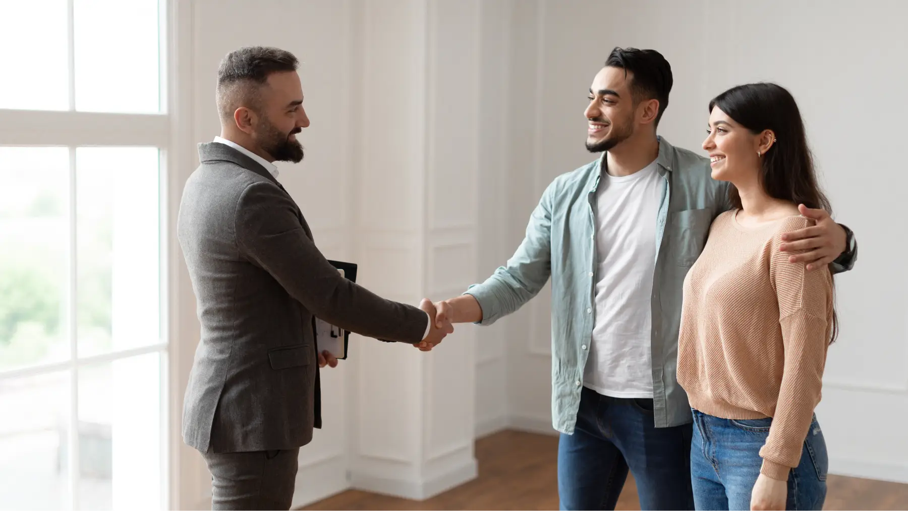 Pareja estrechando la mano de un agente en una vivienda, representando la venta de una propiedad heredada.