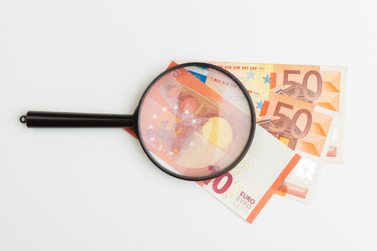 Lupa enfocant bitllets d'euro, representant estratègies per invertir diners amb intel·ligència.