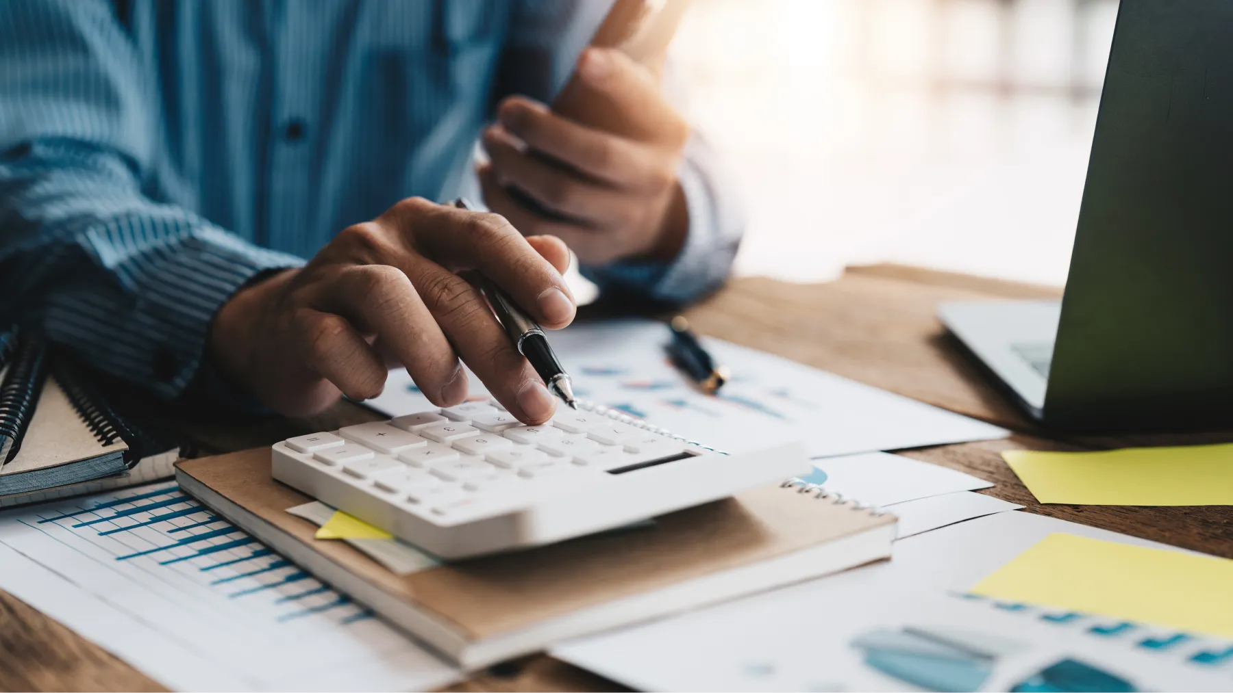 Persona fent servir la calculadora mentre revisa documents financers en una taula amb un pot de monedes. 