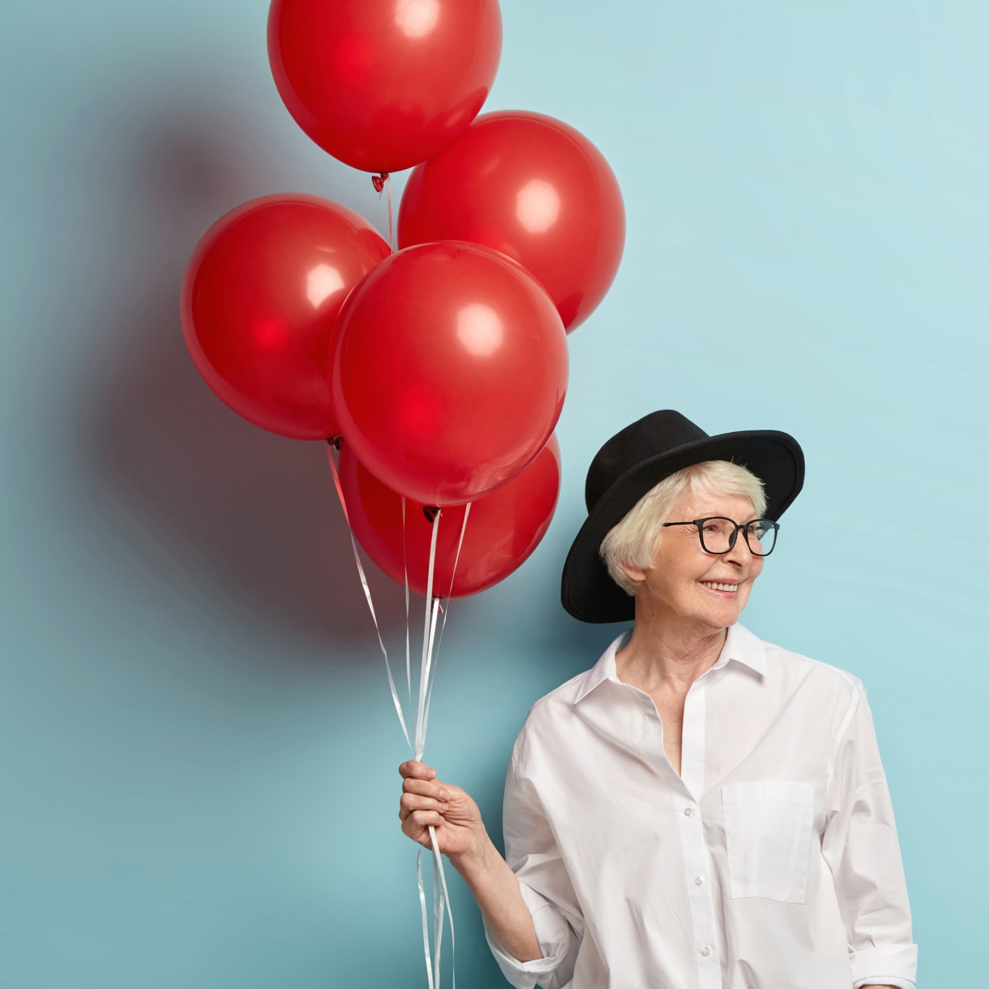 Mujer mayor sonriente con globos rojos, representando la posibilidad de jubilarse a los 60 años. 
