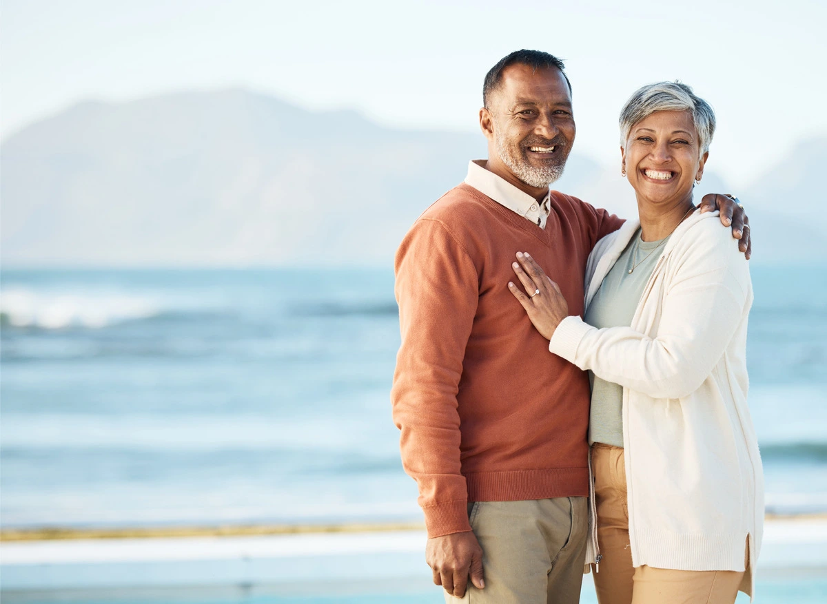 Pareja sonriendo abrazada frente al mar, disfrutando su jubilación ordinaria