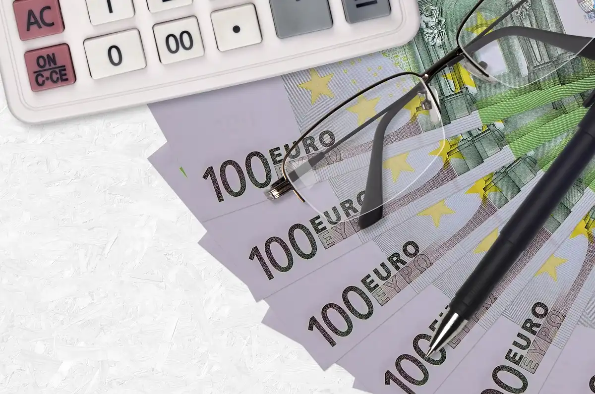 Bolígrafo, calculadora y gafas sobre billetes de 100 euros simbolizando la reforma de pensiones MEI.
