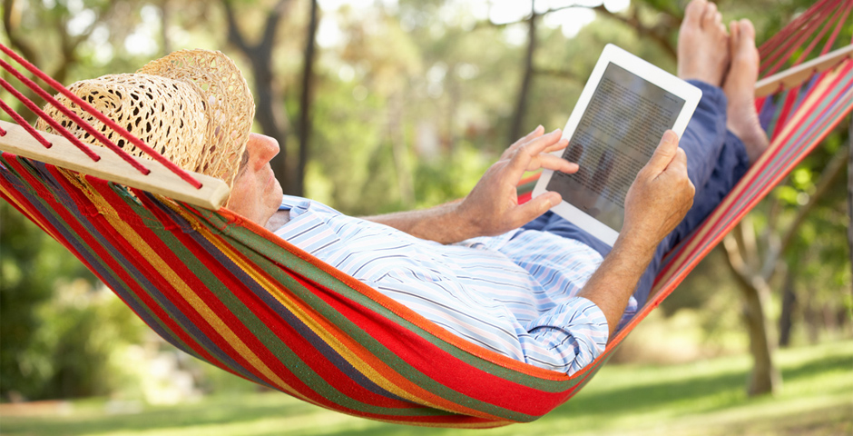 Hombre jubilado leyendo en una hamaca bajo el sol en un entorno tranquilo.