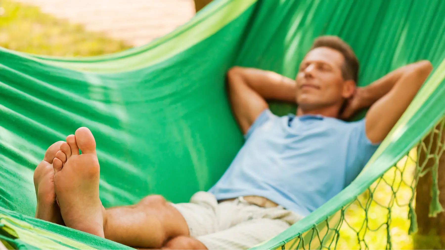Hombre jubilado leyendo en una hamaca bajo el sol en un entorno tranquilo.
