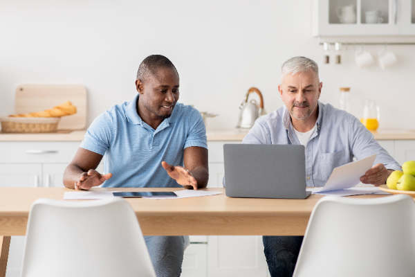 Dos homes revisen documents i una declaració de renda davant d'un ordinador.