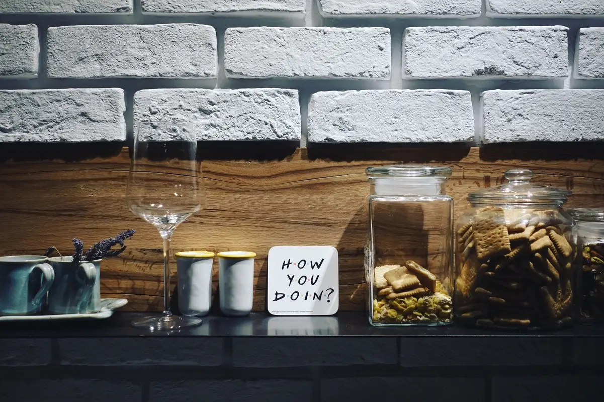 Vasos, tazas y galletas junto a un cartel con frase icónica de Friends sobre dinero y vida.