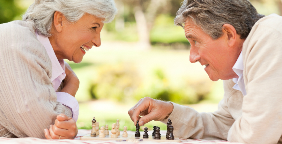 Pareja mayor jugando al ajedrez al aire libre, disfrutando de ventajas fiscales para mayores de 65 años.