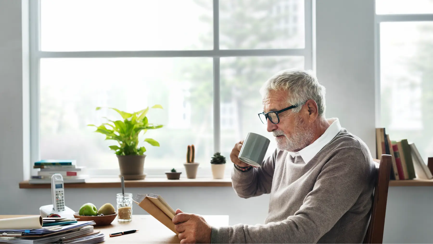 Hombre mayor leyendo documentos mientras toma café, revisando pensión de jubilación y viudedad.