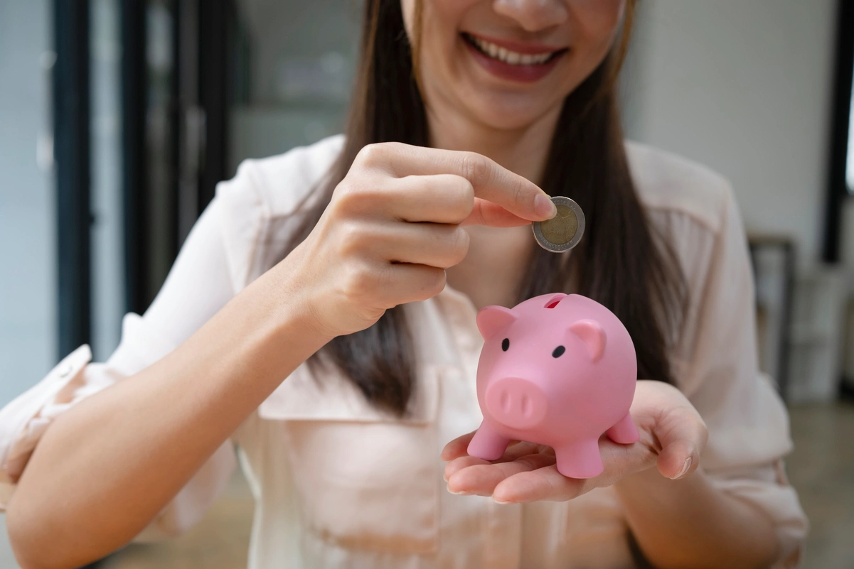 Mujer depositando moneda en alcancía rosa, representando la propensión marginal al ahorro.