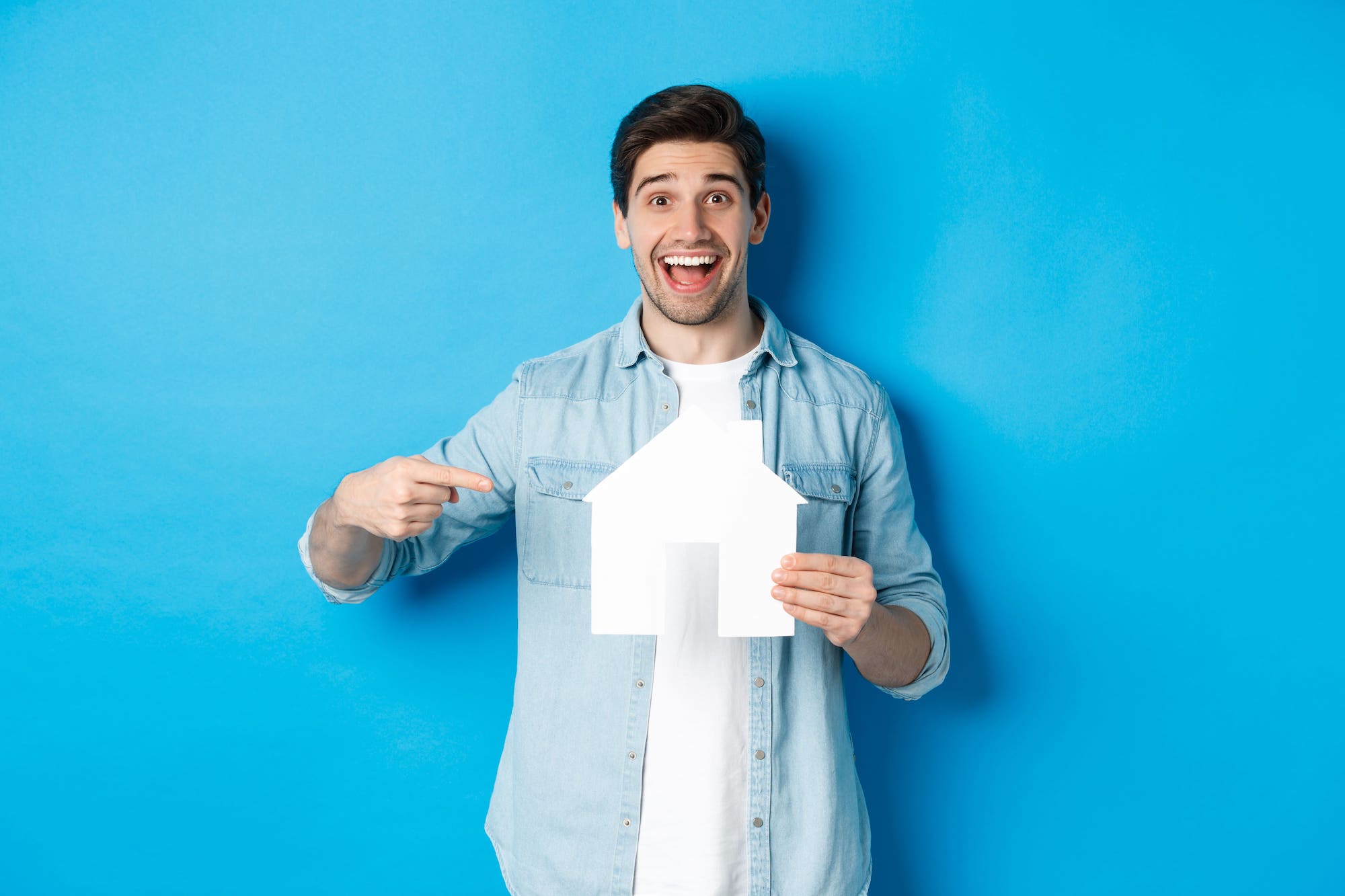 Home somrient assenyalant una casa de paper en referència a conceptes financers com la TAE.