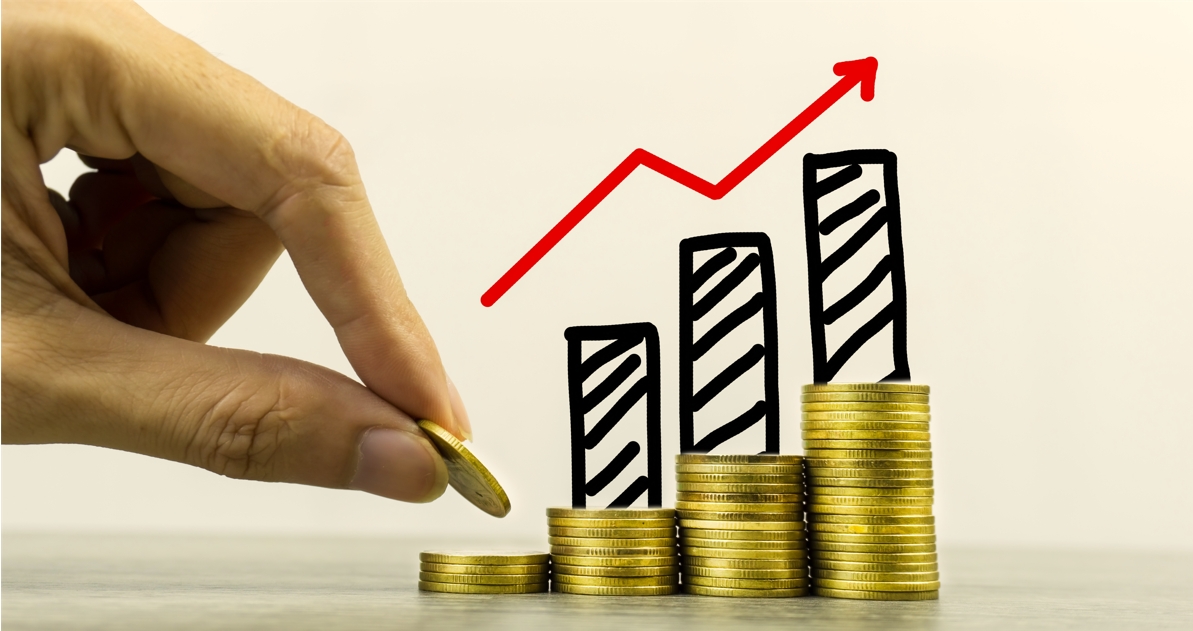 Mano apilando monedas sobre una mesa con un gráfico ascendente que representa fondos de inversión.