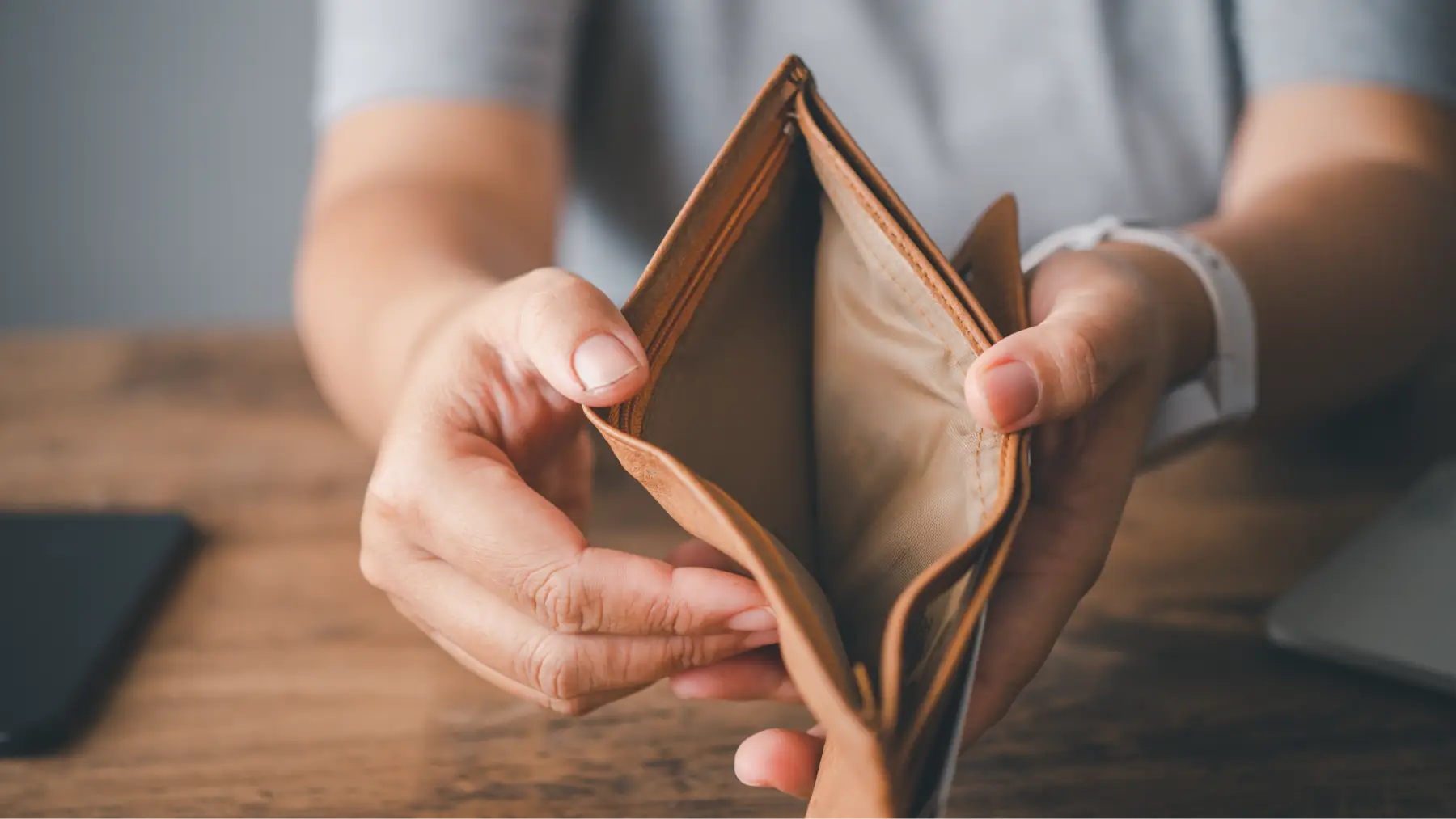 Manos sosteniendo una billetera vacía frente a un portátil, simbolizando necesidad económica.