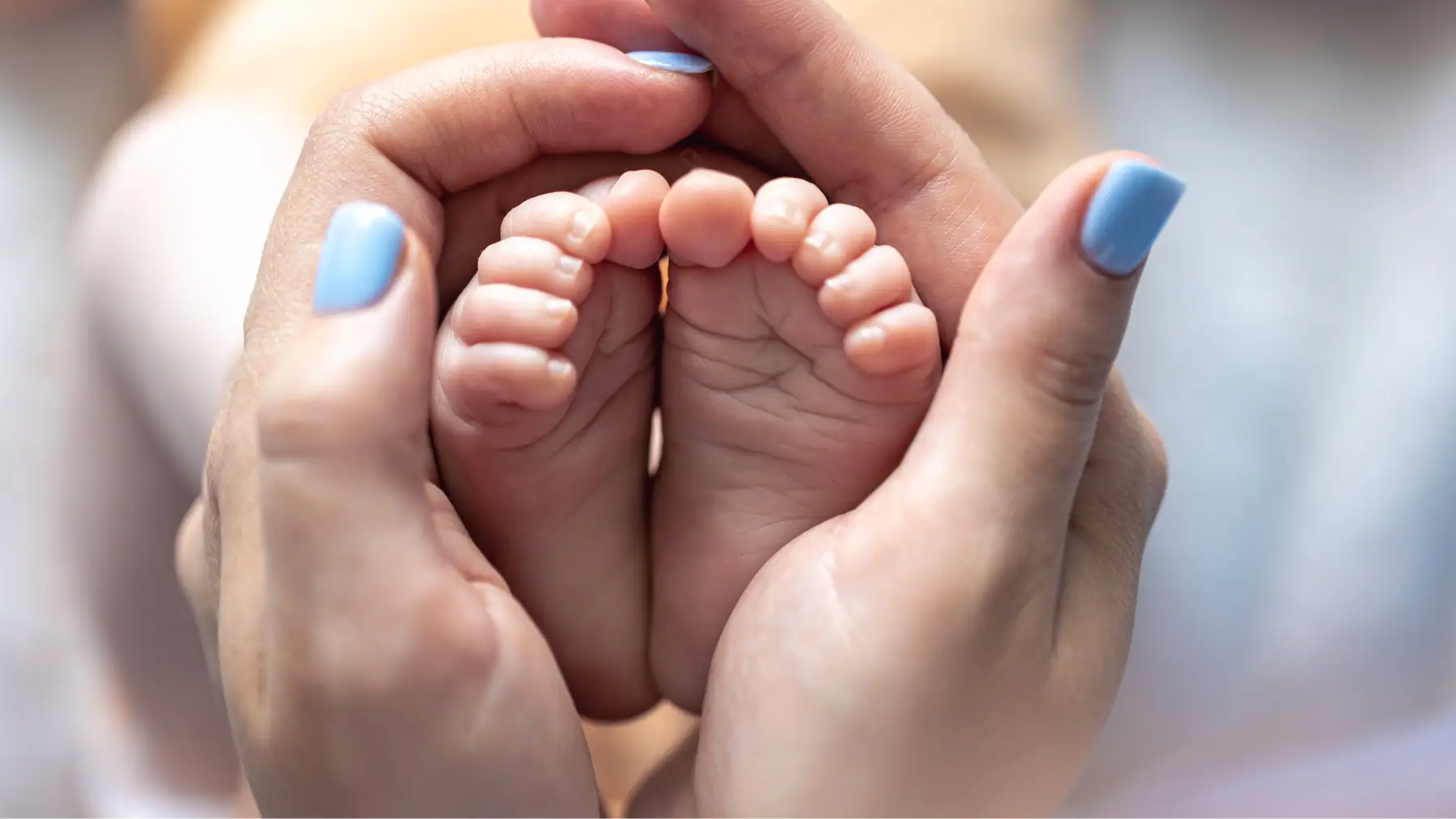 Primer plano de manos adultas sosteniendo los peques de un bebé, simbolizando la protección familiar de un seguro de vida.