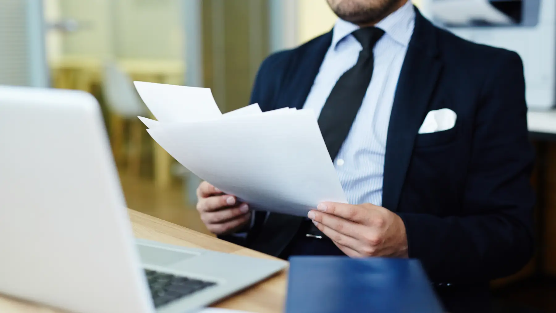 Hombre con traje revisando documentos en oficina, representando el proceso de elaboración de un testamento vital.