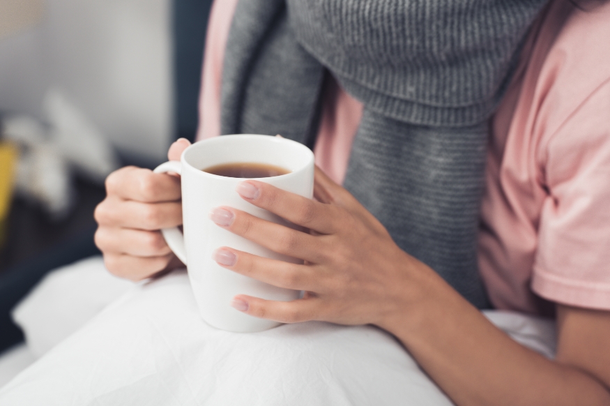Persona con bufanda sosteniendo una taza de té, representando reposo por baja laboral.