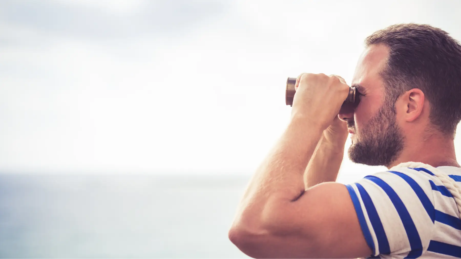 Hombre mirando al horizonte con un catalejo al mar, representando a los trabajadores del mar.