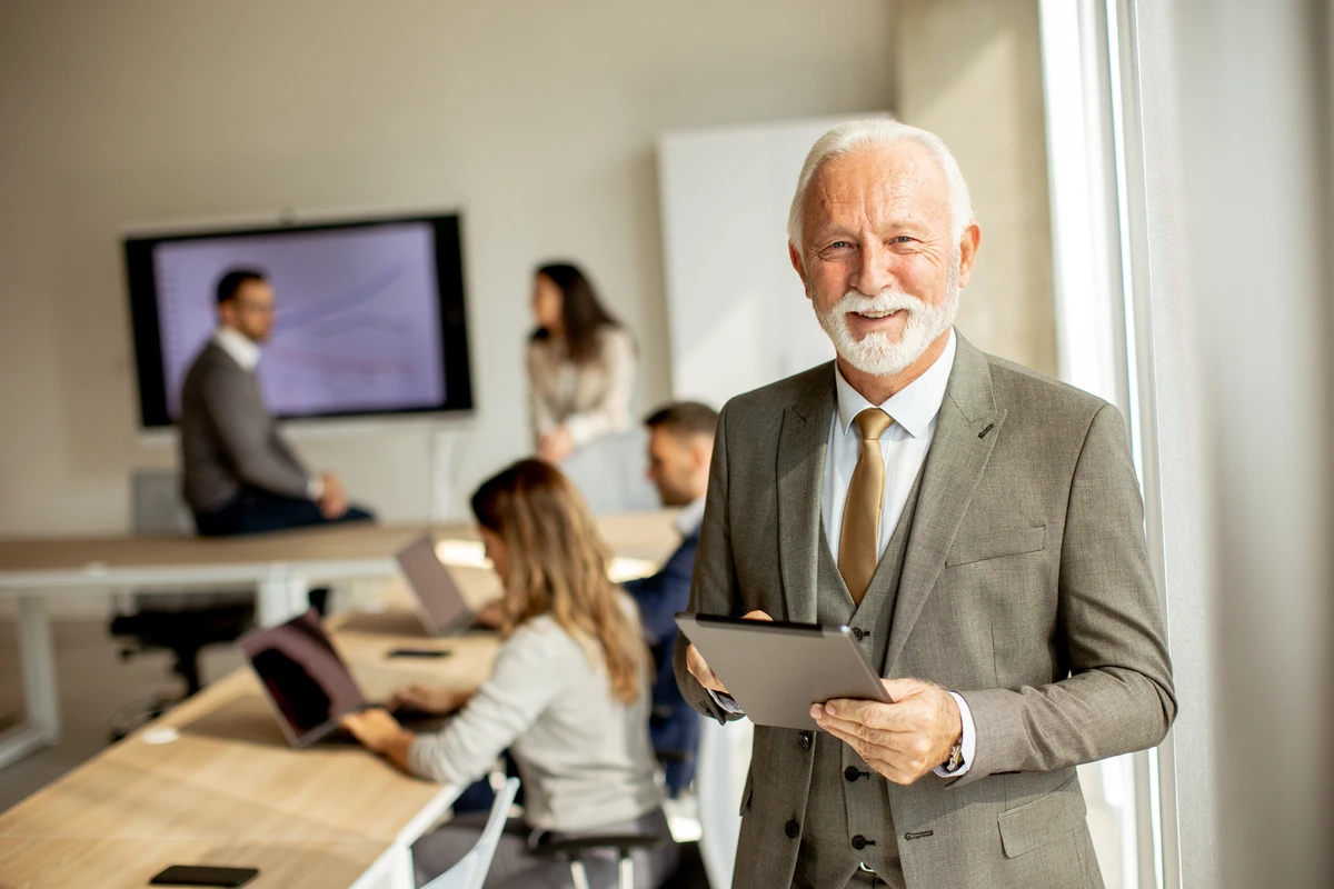 Profesional sénior sonriente con una tablet en una reunión de upskilling empresarial
